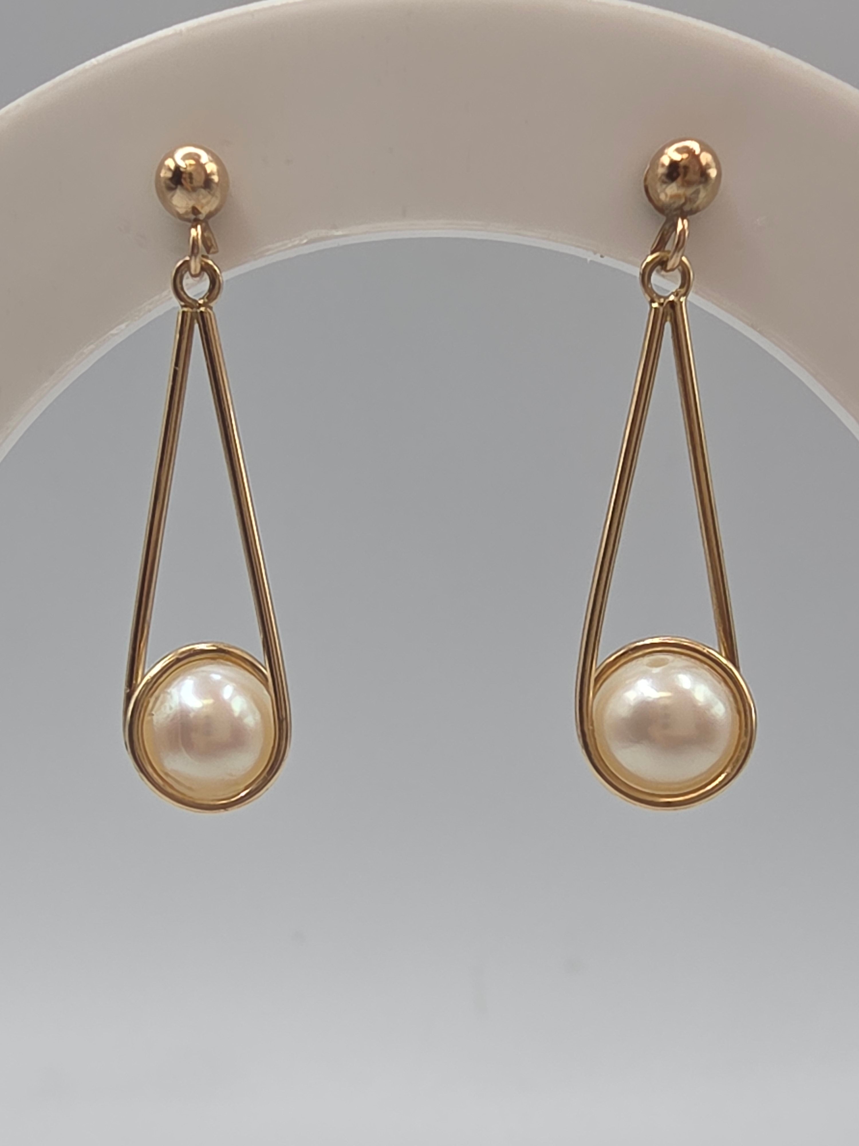 Solid 14K yellow gold pearl dangle earrings with elongated teardrop wire frames and ball post tops